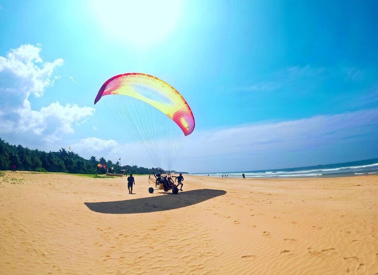A beach with a parasail in the air, people on the sand, and the ocean in the background. 5