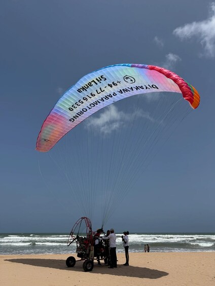 A paraglider with a rainbow-colored canopy preparing for takeoff on a beach. 2