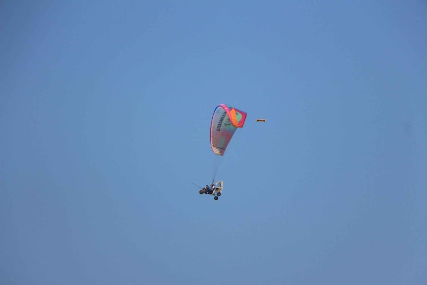 A paraglider with a colorful canopy flying against a clear blue sky. 4