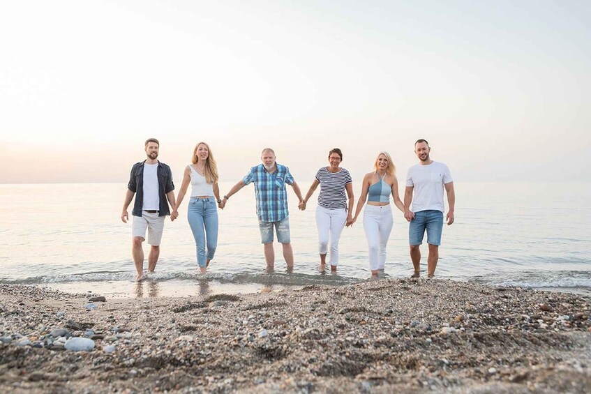 A group of people holding hands walking along a pebbly beach. 1