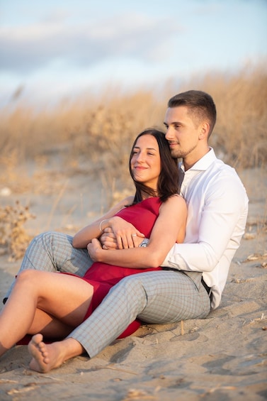 A couple sitting on a sandy beach with dry grass in the background. 5