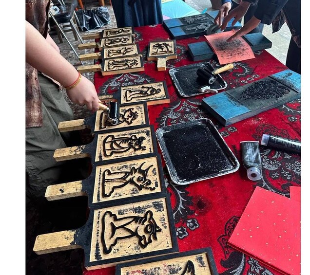 A person carving wooden blocks with designs, tools, and materials on a table. 4