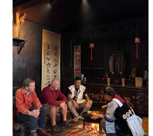 A group of people seated around a traditional stove in a dimly lit room with wooden walls and decorative elements. 3