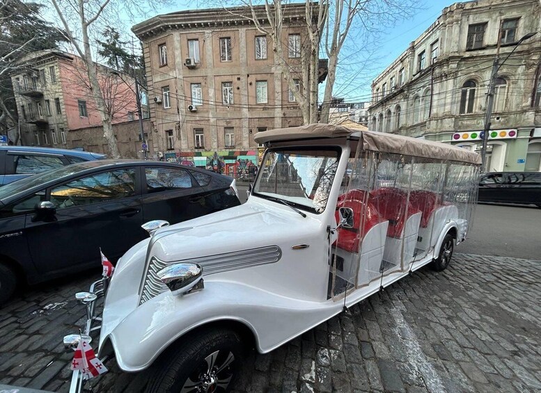 A vintage white car with a transparent side panel parked on a cobblestone street. 5