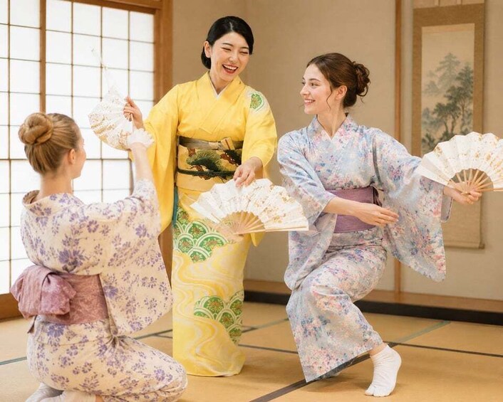 Three people in traditional Japanese attire performing a fan dance in a room with tatami flooring and a shoji screen. 1