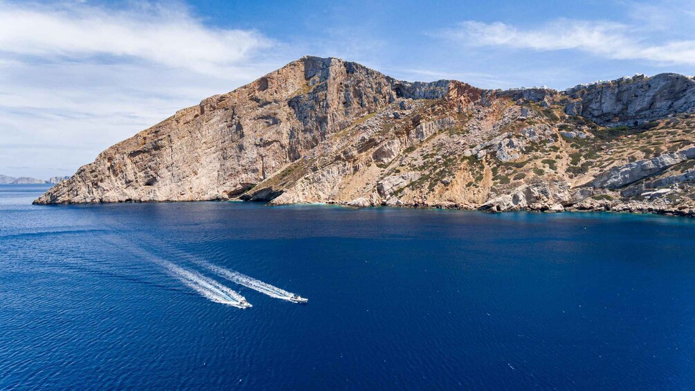 A mountainous coastline with a clear blue sea and a boat creating a wake. 2