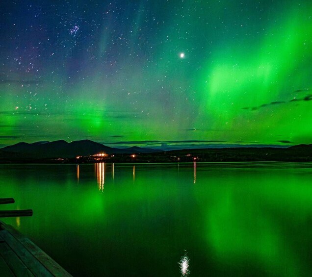 A night sky with the aurora borealis reflected in a calm body of water, with mountains in the background. 1