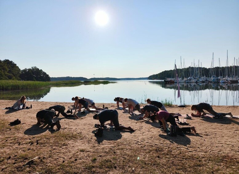 A group of people performing yoga on a sandy beach with a calm lake and sailboats in the background. 5