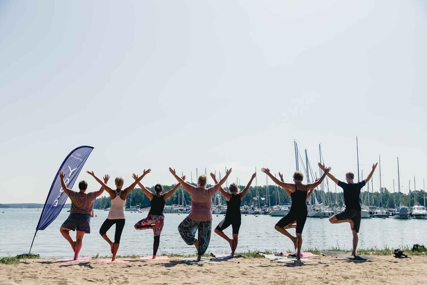 A group of people performing yoga on a beach with a marina in the background. 3