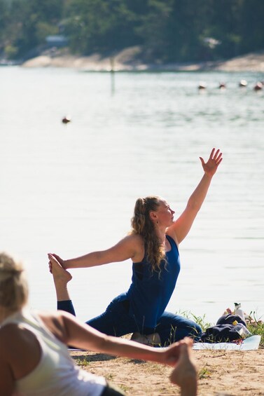 A person performing yoga on a sandy beach with a calm body of water and greenery in the background. 4