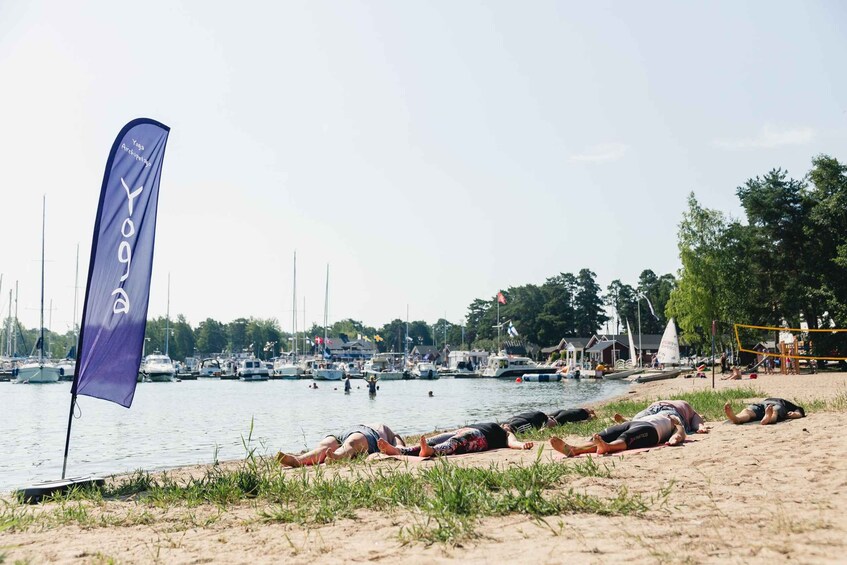 A beach with people sunbathing, a sailboat, and a purple flag. 1