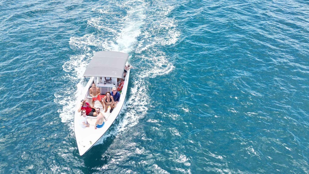 A white boat with people on board, moving through clear blue water. 1
