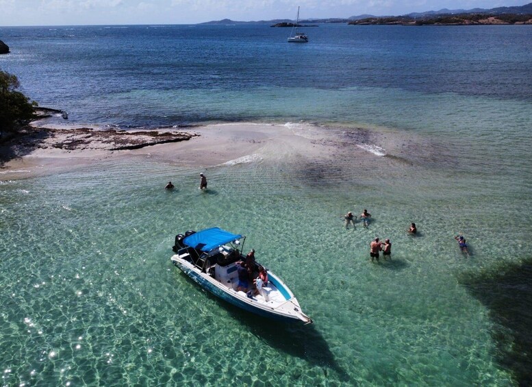 A boat with people on a clear blue sea, a sandy beach, and a distant sailboat. 2