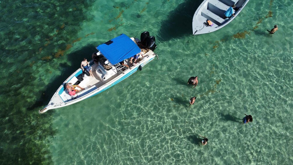 A boat with people on it and others swimming in clear water. 3