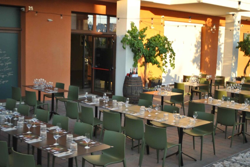 An outdoor dining area with tables set for a meal, green chairs, and a large barrel. 3