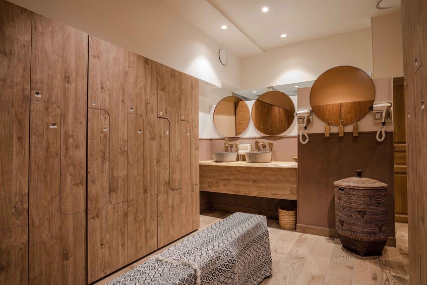 A modern bathroom with wooden cabinets, a bench, a round mirror, and a hairdryer. 2