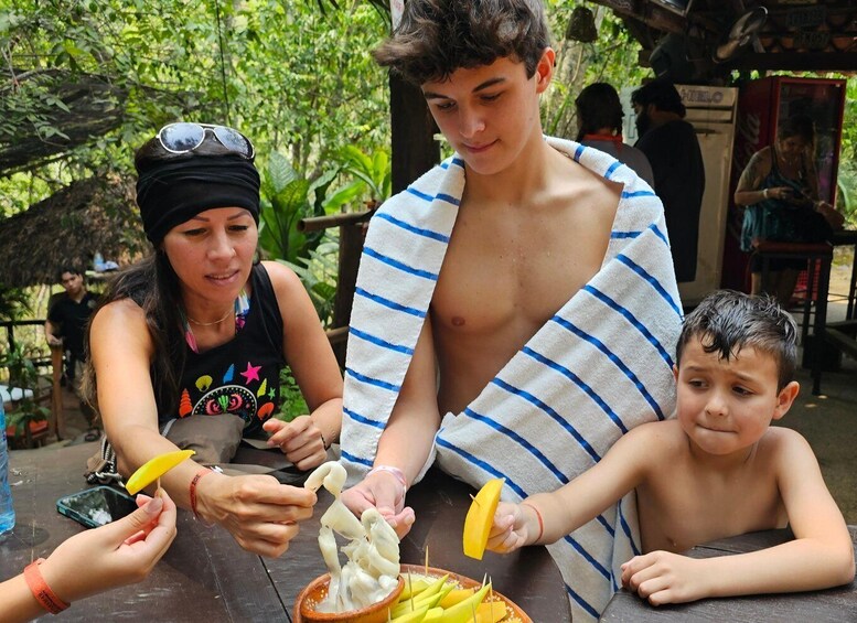 People preparing food outdoors, with a tropical setting and a thatched-roof structure in the background. 4