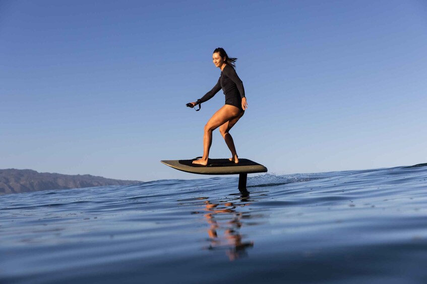 A person surfing on a calm ocean with clear skies and distant landforms. 1