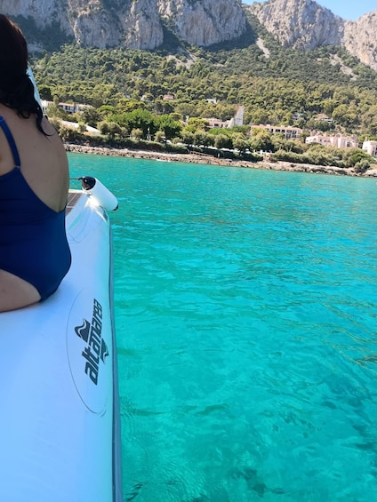 A person in a blue swimsuit on a boat with clear turquoise water, rocky cliffs, and greenery in the background. 3