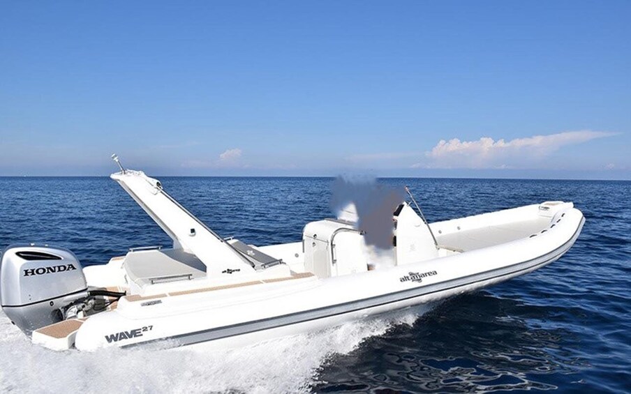A white motorboat with 'HONDA' and 'WAVE 27' on the side, moving through calm blue water under a clear sky. 1