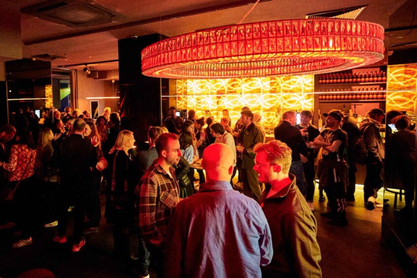 A crowded indoor event with a circular red light fixture and patterned wall decorations. 5