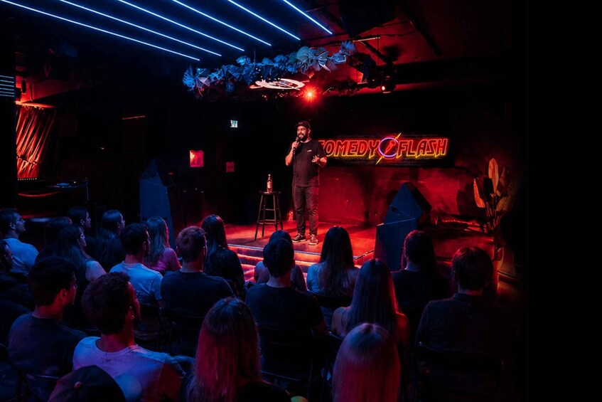 A stage with a neon sign reading 'COMEDY FLASH' and a performer. 2