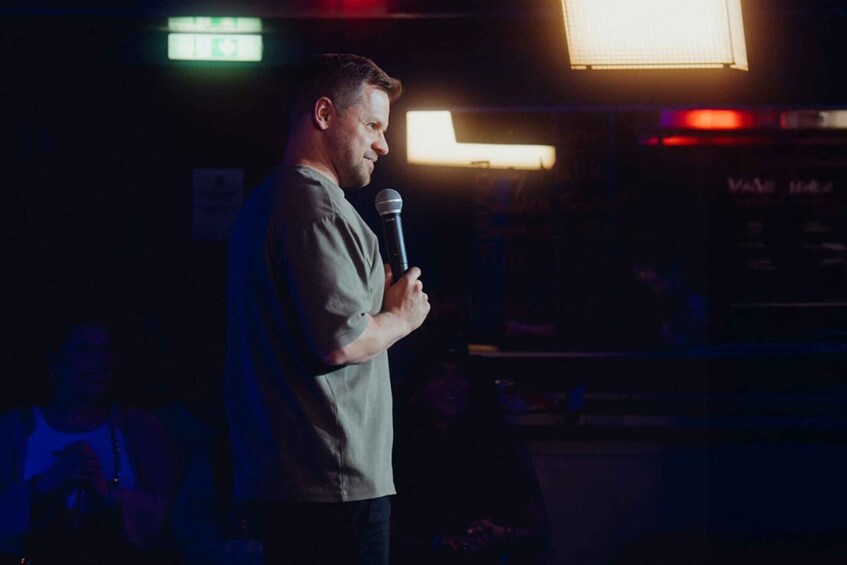 A person holding a microphone, standing in a dimly lit room with a sign that reads 'EXIT' in the background. 4
