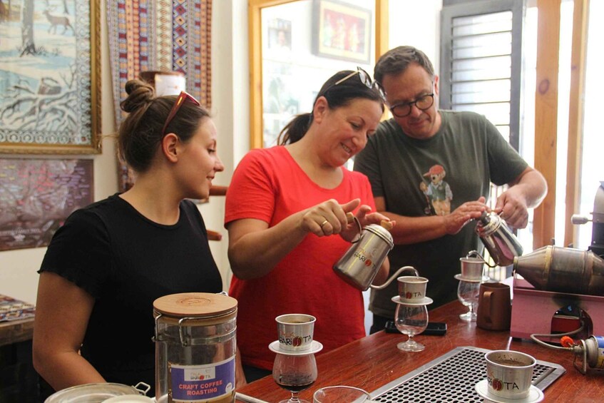 Three people at a coffee station with a coffee press, cups, and a jar labeled 'CRAFT COFFEE ROASTING.' 5