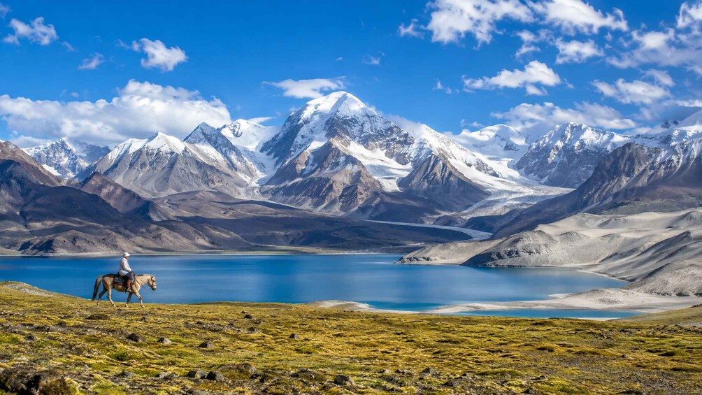 A person riding a horse across a mountainous landscape with a lake. 1