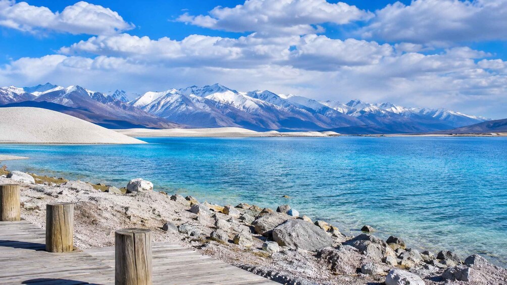 A clear lake with a wooden dock, snow-capped mountains in the background, and a clear sky. 3