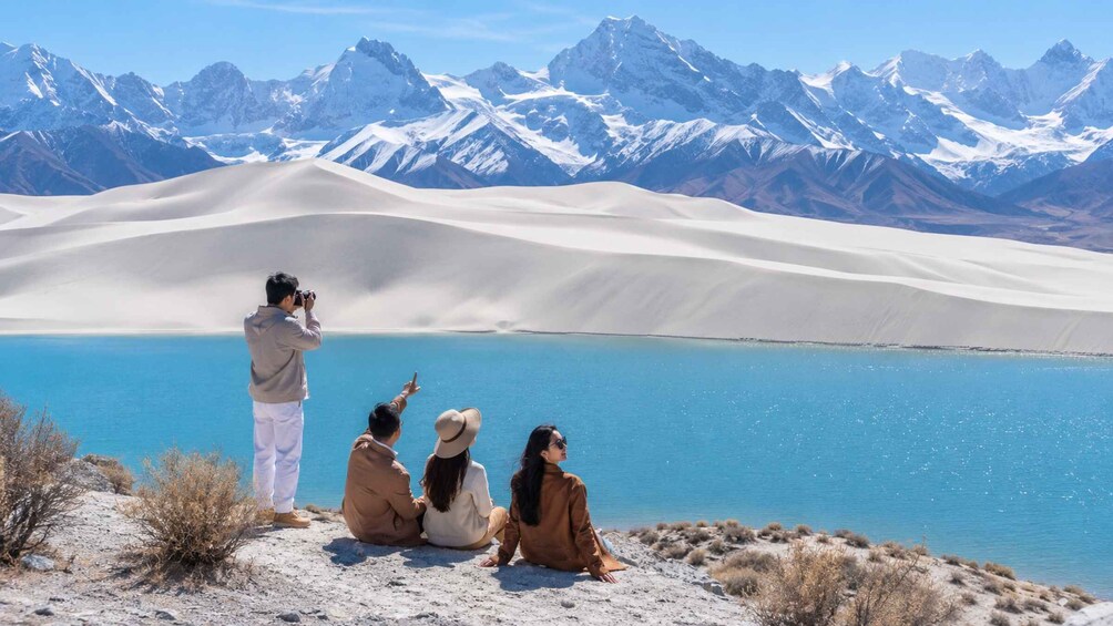 A group of people sitting by a lake with mountains in the background. 4