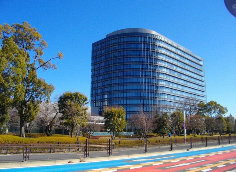 A modern curved building with reflective glass windows, surrounded by a park with trees and a pedestrian walkway. 1
