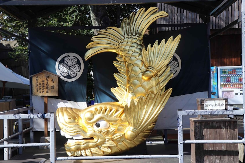 A large golden fish sculpture with a shrine in the background. 3