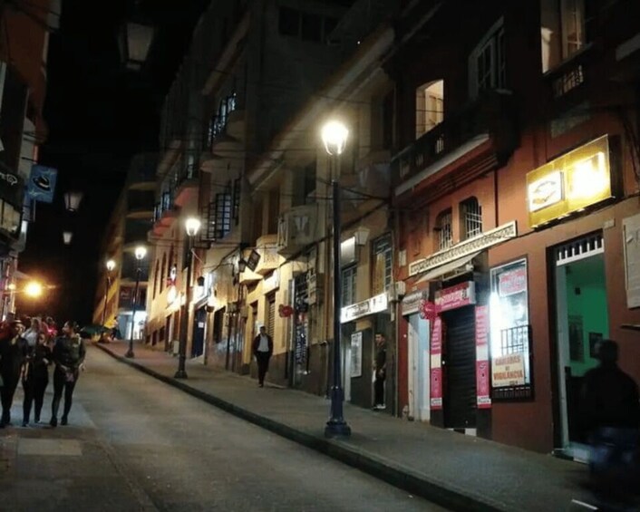 A nighttime street scene with illuminated storefronts and a few pedestrians. 2