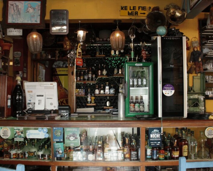 A bar with shelves of liquor bottles, a refrigerator, and hanging lights. 1