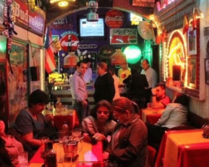 A crowded indoor bar with neon signs and people sitting at tables. 3