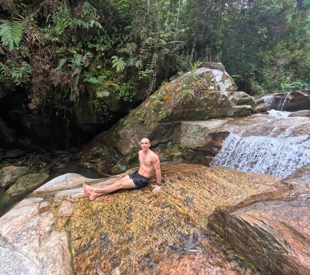 A person sitting on a rock by a waterfall in a forested area. 1