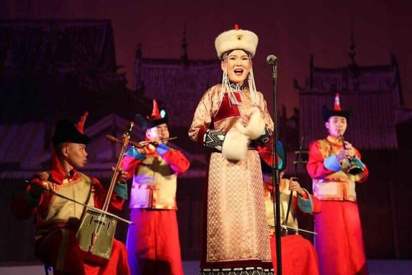 A person in traditional attire with a microphone, flanked by individuals playing stringed instruments. 1