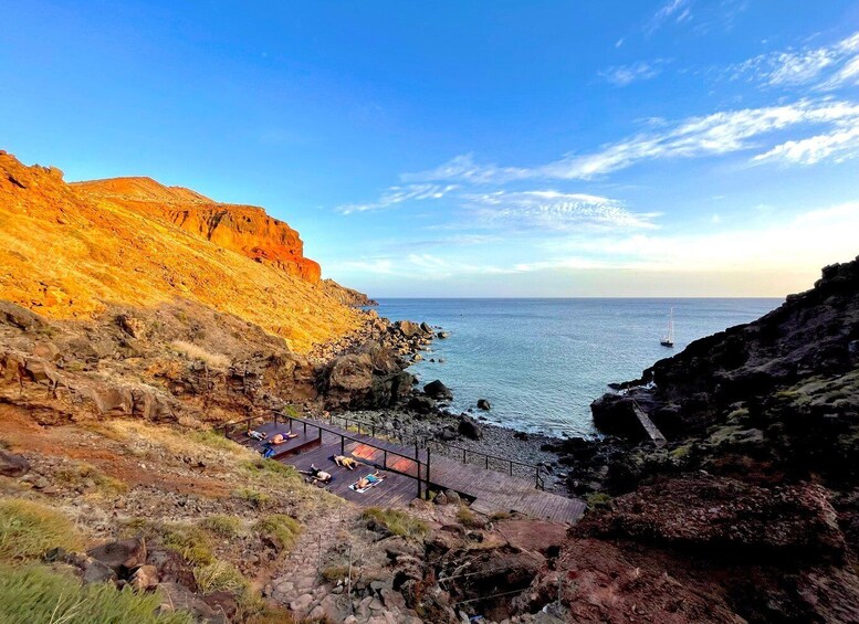 A coastal landscape with cliffs, a wooden walkway, and a sailboat in the distance. 1