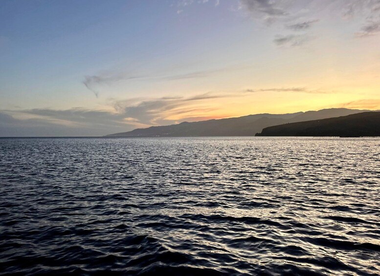 A calm sea with a sunset, distant mountains, and a clear sky. 2