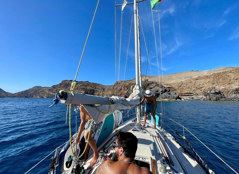 A sailboat with two people on deck, rocky coastline in the background, and calm blue waters. 4