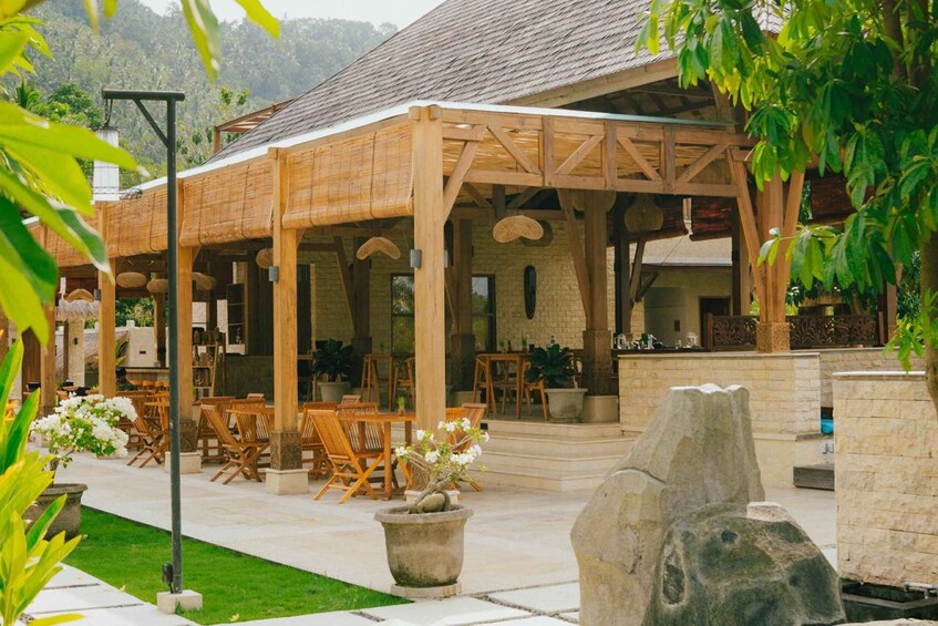 An outdoor wooden structure with tables and chairs, surrounded by greenery and stone features. 4
