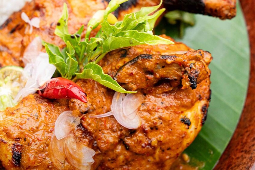 Grilled chicken with a spicy marinade, garnished with red chili, onion slices, and green herbs. 2
