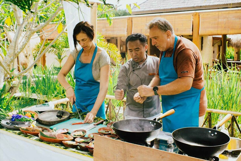 Three people cooking outdoors with a variety of dishes and cooking utensils. 1