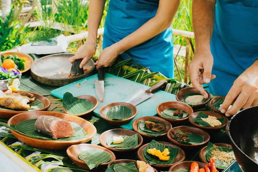 A person preparing food with a knife and cutting board, surrounded by bowls with food on banana leaves. 3