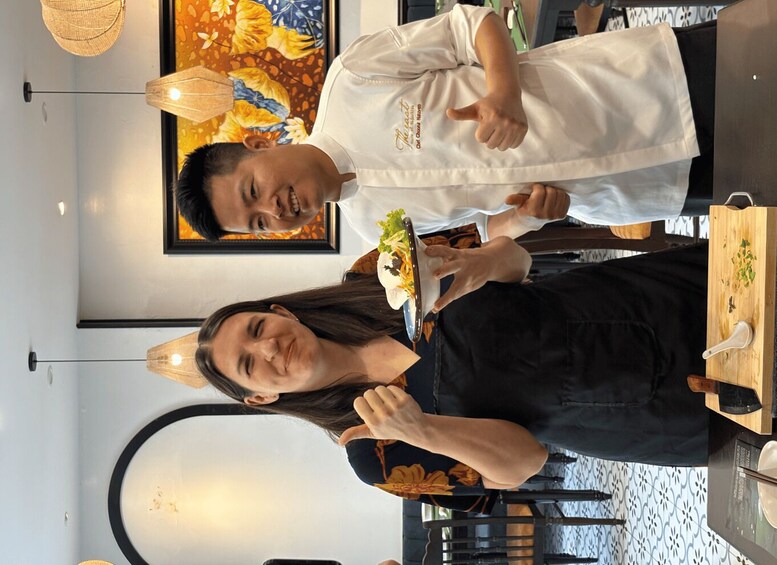 Two people standing in a restaurant with a table, chairs, and a decorative wall. 5