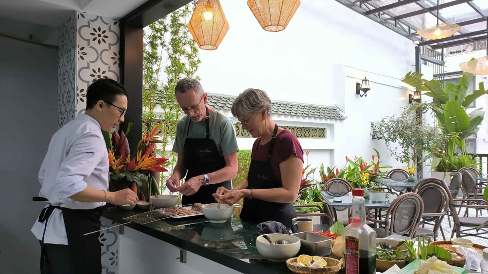 Three people preparing food at an outdoor restaurant with a variety of ingredients and utensils on the counter. 1