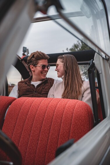 Two people sitting in a convertible car with red seats. 4