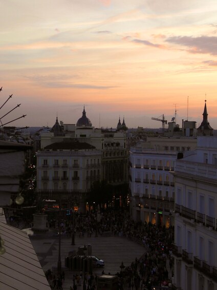 A cityscape at dusk with prominent domed buildings and a bustling square. 4