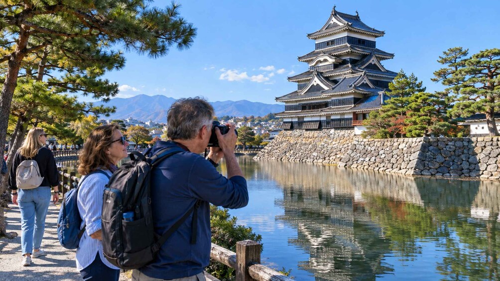 A traditional Japanese castle by a calm lake with tourists taking photos. 2